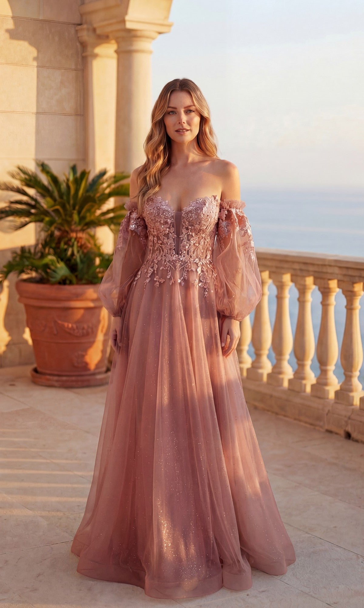 A woman stands on a balcony with ocean and plants in the background, wearing the Chicas C358 Long Formal Dress in rose—an off-the-shoulder gown featuring sheer sleeves and floral embroidery.